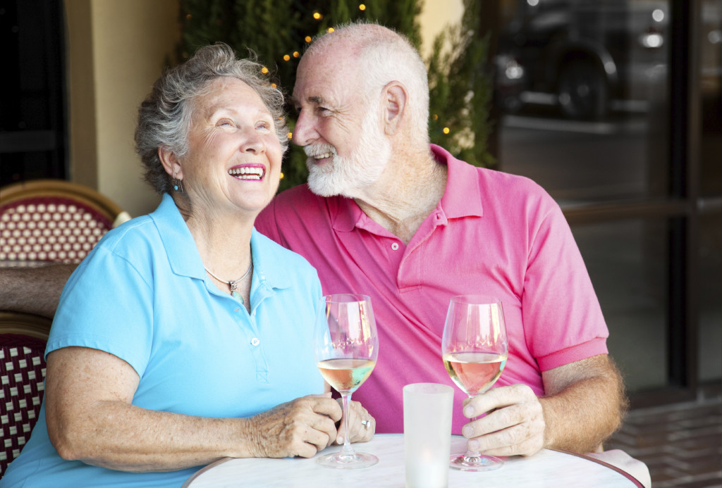 Uśmiechnięci dziadkowie przy stoliku w restauracji piją białe wino
