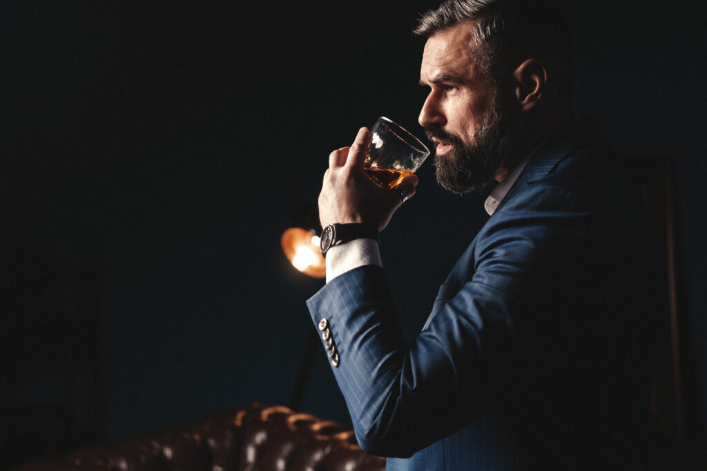Jak wybrać whisky? Whisky a koniak - mezczyzna w ciemnym pomieszczeniu przechyla szklaneczke z whisky