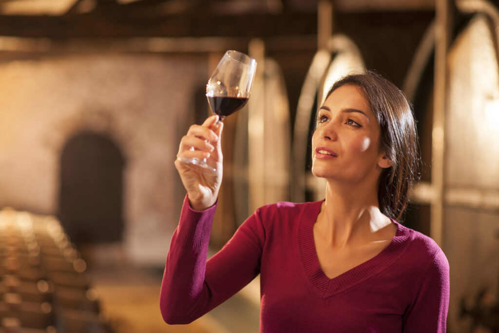 Degustacja czerwonego wina, kobieta z uniesionym kieliszkiem w winnicy
