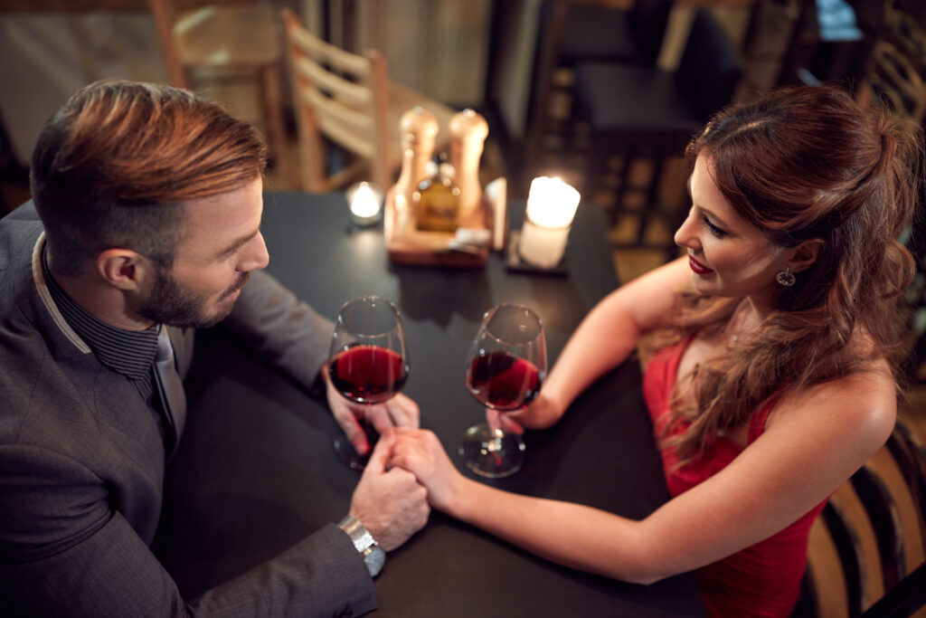 Romantyczna kolacja, para przy stoliku ze świecami pijąca czerwone wino.