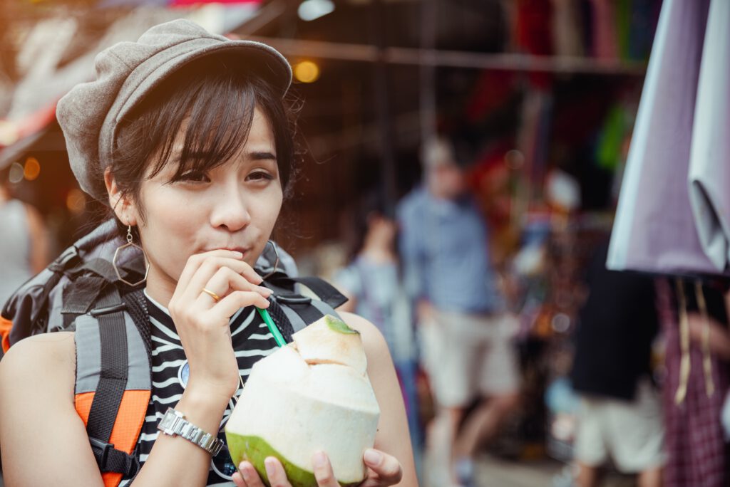 Kobieta o azjatyckiej urodzie pije coś z kokosa.
