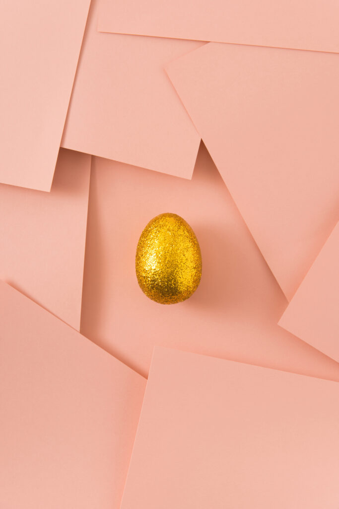 Gold easter egg on powder pink background. Minimal creative composition. Flat lay.