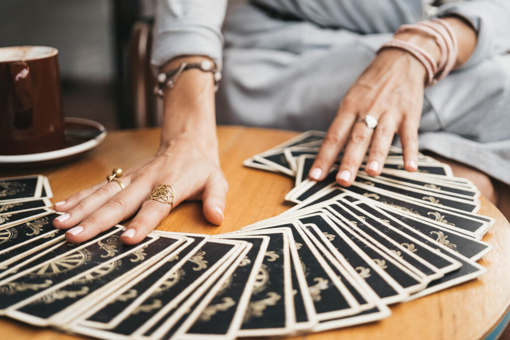 Andrzejki: talia kart rozłożonych na stole, kobiece ręce z pierścionkami, obok kart kubek.