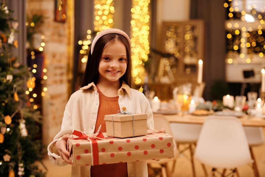 Prezenty na Święta dla dzieci - zdjęcie uśmiechniętej dziewczynki trzymającej dwa prezenty