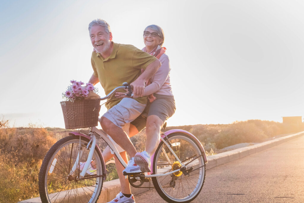 Dzień Babci i Dziadka - starsza para jedzie na rowerze z koszykiem, w którym są kwiaty