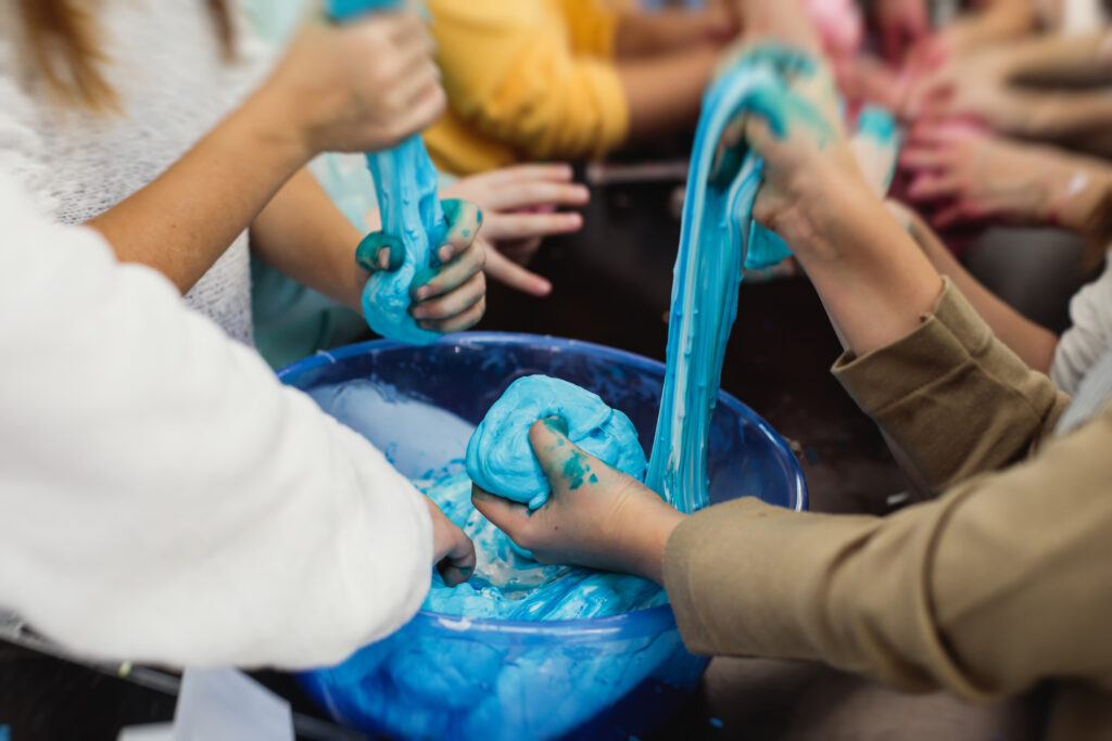 Zajęcia dodatkowe dla dzieci i młodzieży - na zdjęciu lepienie z niebieskiej masy plastelinowej. Zbliżenie na ręce.