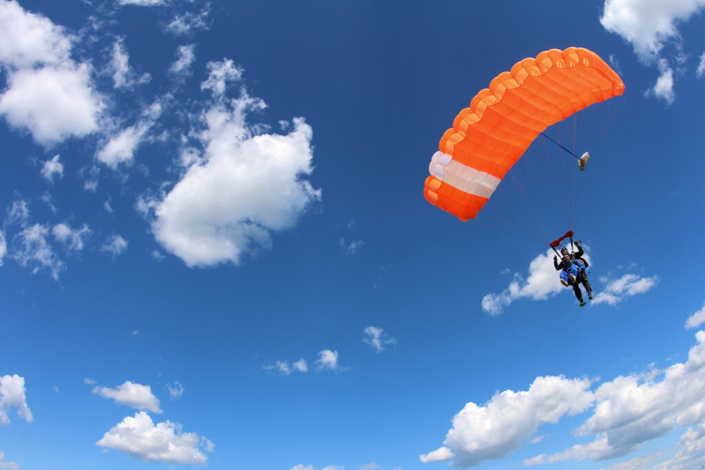 Skok ze spadochronem z instruktorem w tandemie. Czerwono-biały spadochron na tle niebieskiego nieba z chmurami. 