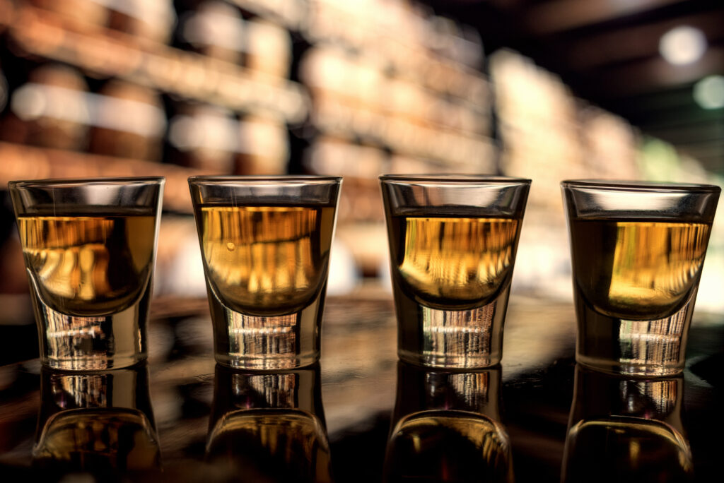 Whisky w 4 szklankach stoi rzędem na stole. W tle bar.