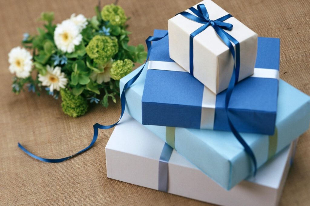 Biało zielony bukiet kwiatów. Niebiesko-białe pudełka prezentowe owinięte kokardkami. 