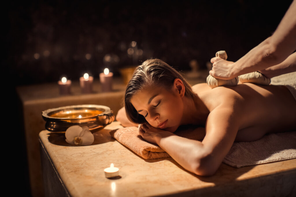 Młoda kobieta odpoczywa podczas masażu. W tle świeczki i klimatyczny wystrój. 