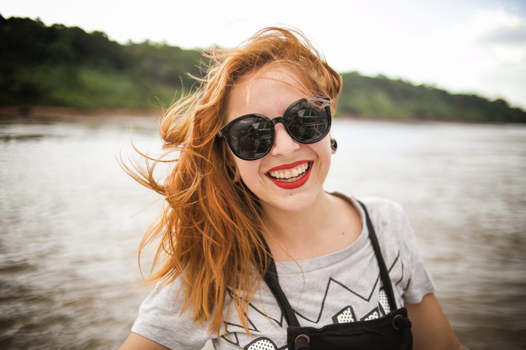 Uśmiechnięta kobieta w okularach przeciwsłonecznych na tle morza. 