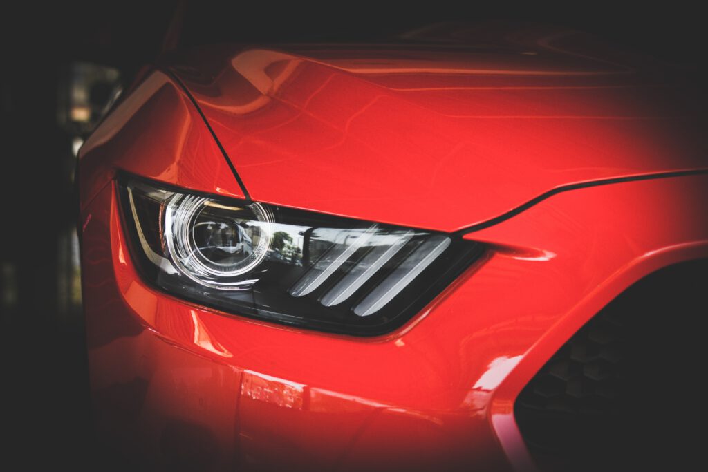Na zdjęciu znajduje się reflektor czerwonego Forda Mustanga w dużym przybliżeniu.