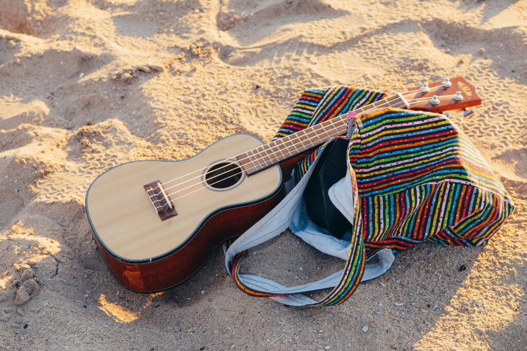 Kolorowa torba leży na plaży. Na niej znajduje się gitara.