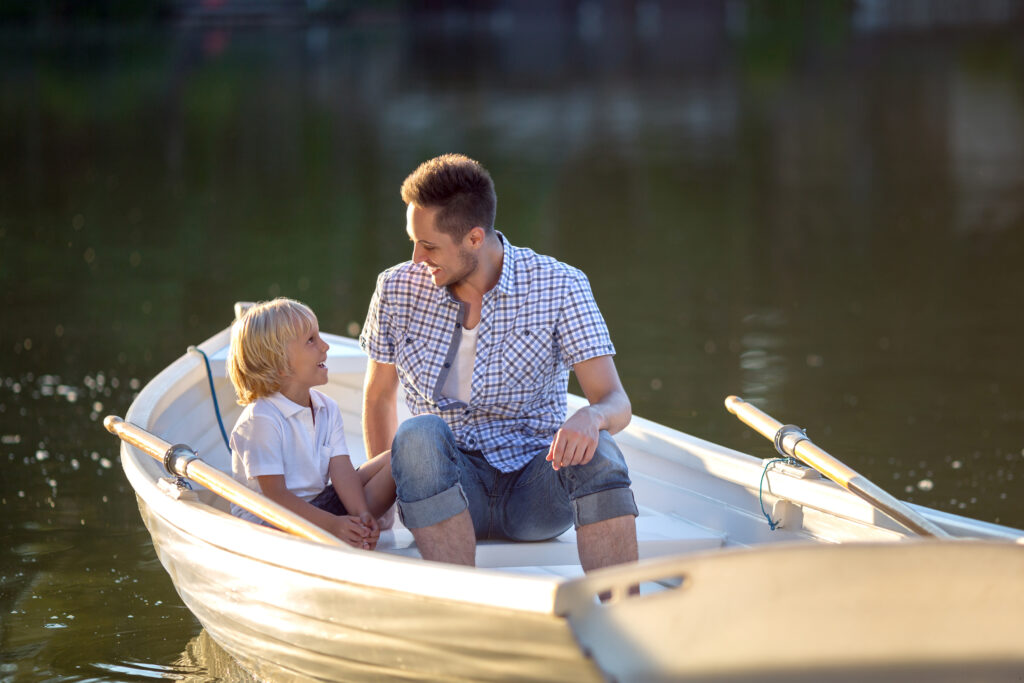 Mężczyzna siedzi z dzieckiem w łódce na jeziorze. Patrzą się na siebie.