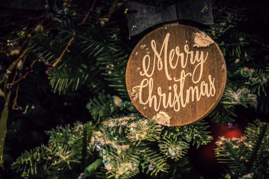 Drewniana bombka z napisem ,,Merry Christmas" wisi na choince.