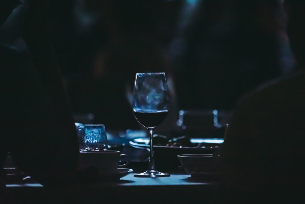 Kieliszek wina razem z talerzami stoi na stole. Ciemna kolorystyka.